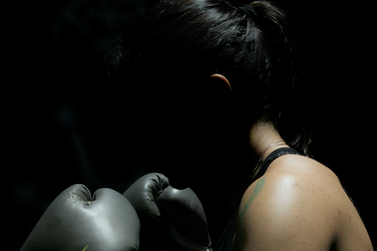Silhouette d'une boxeuse dans l’ombre, en position de garde avec des gants, éclairée subtilement sur l'épaule et la nuque, créant une ambiance intense et introspective.